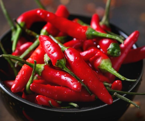 Black bowl of wet fresh red hot chili peppers and dry chilli flakes over old wooden textured background. Spicy theme. Close up with selective focus