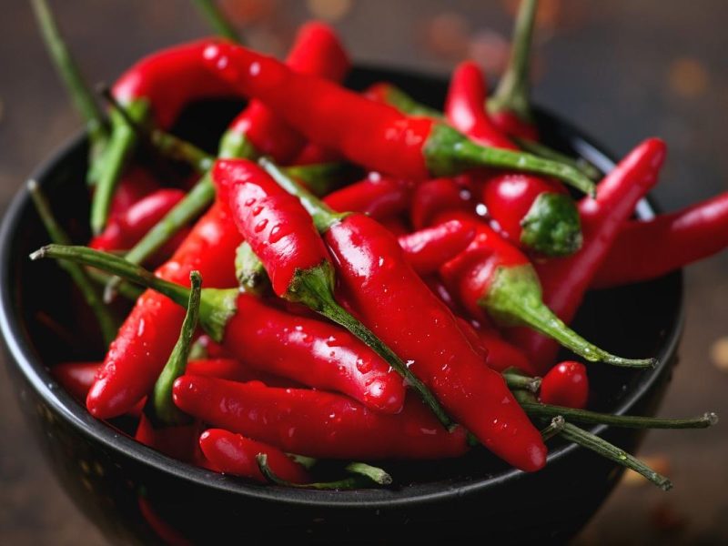 Black bowl of wet fresh red hot chili peppers and dry chilli flakes over old wooden textured background. Spicy theme. Close up with selective focus